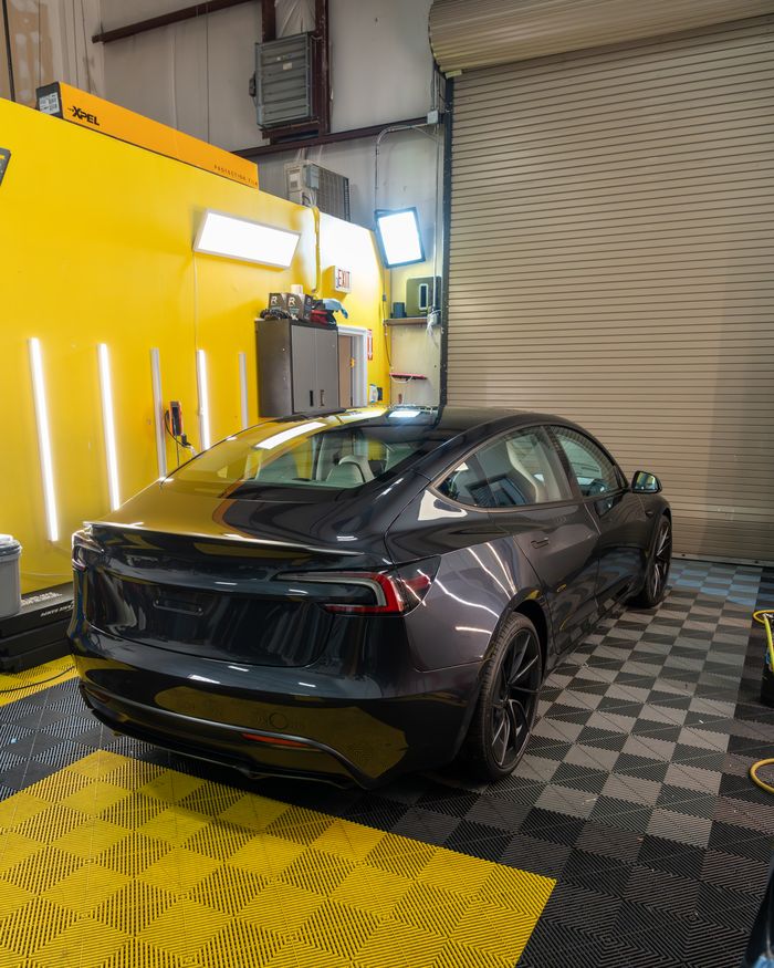 A grey Tesla Model 3 against the yellow bay wall