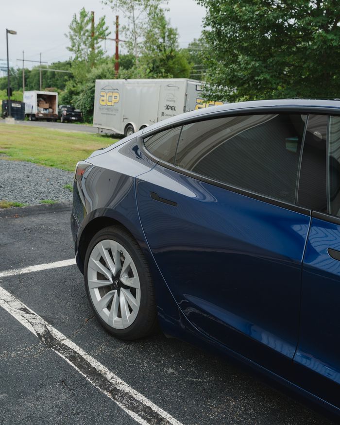 A blue Tesla Model 3 with dark tinted rear glass and ACP trailer behind