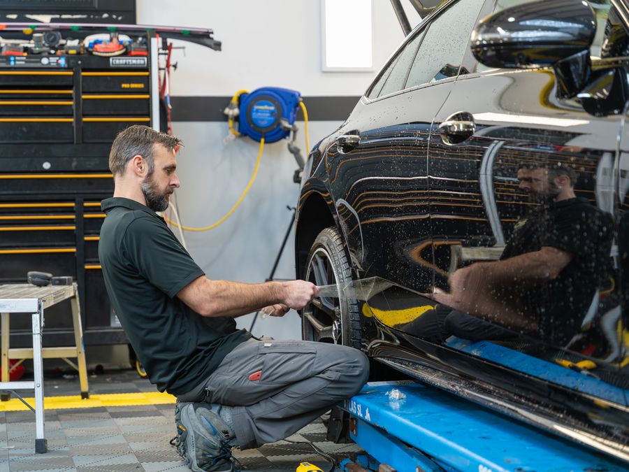 An ACP technician fitting film along the lower door of a black car