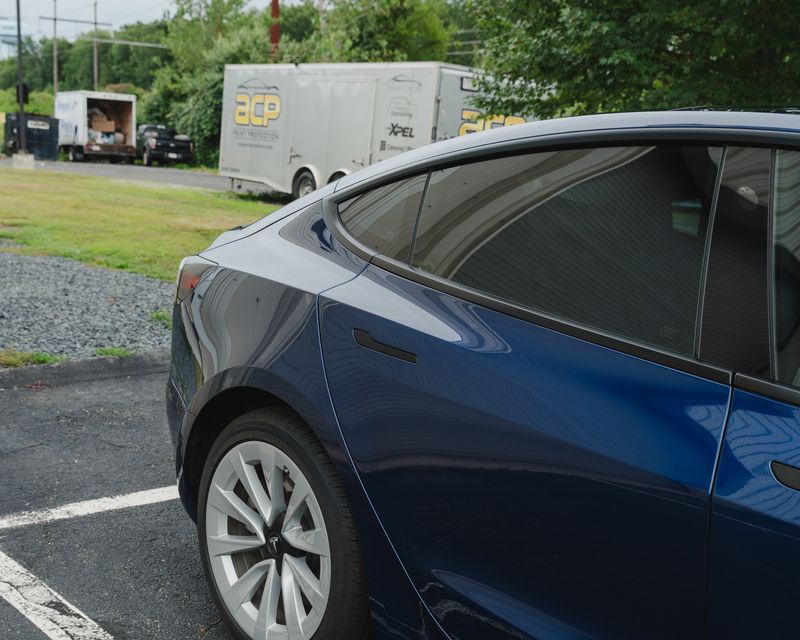 The dark tinted rear glass of a blue Tesla Model 3